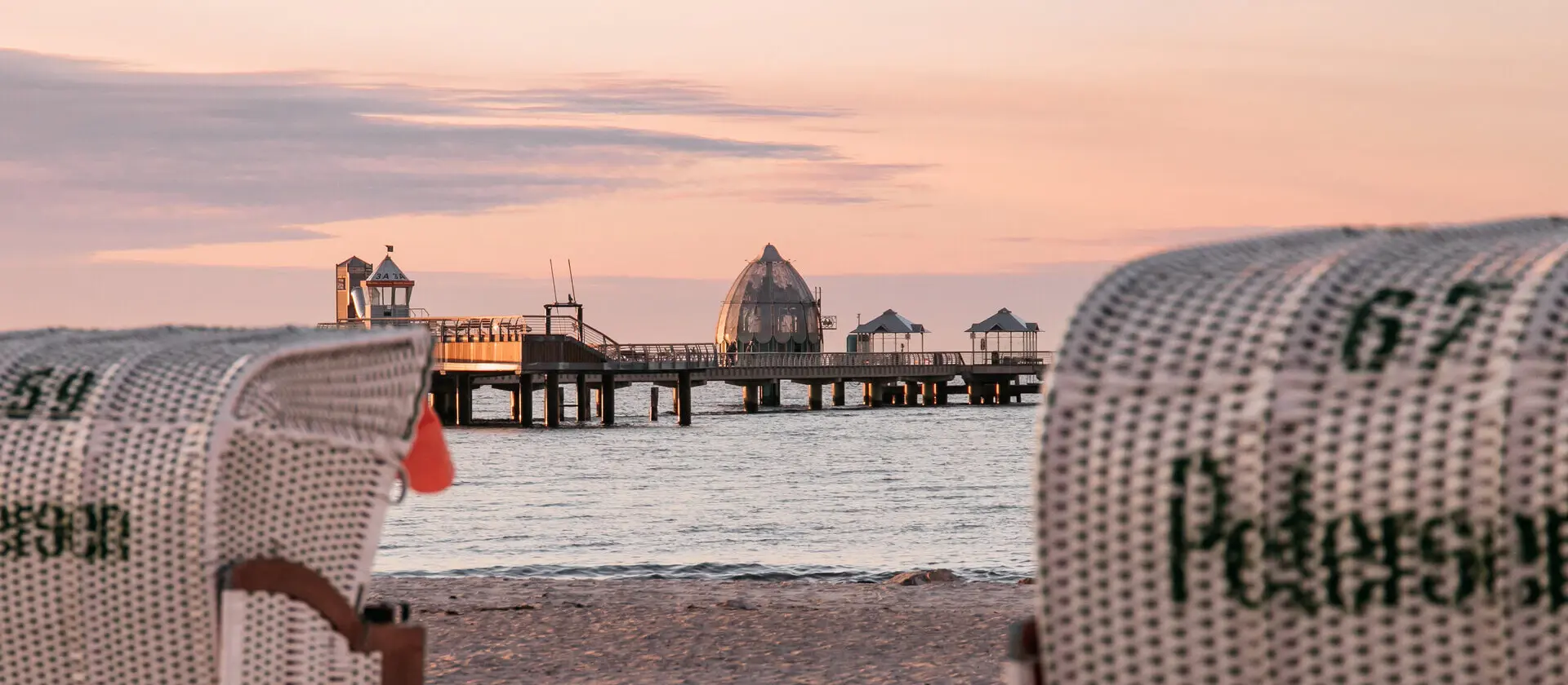 Strandkorb am Strand mit einem Pier im Hintergrund