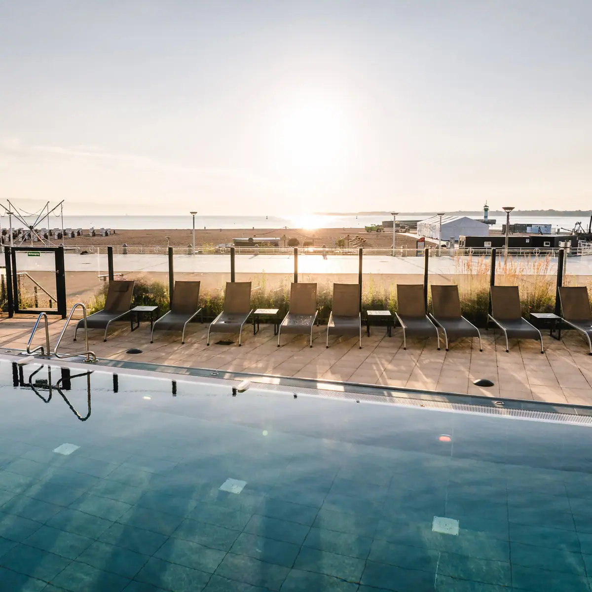 Außenpool mit Strandblick Ein Pool mit Stühlen und einem Strand im Hintergrund.