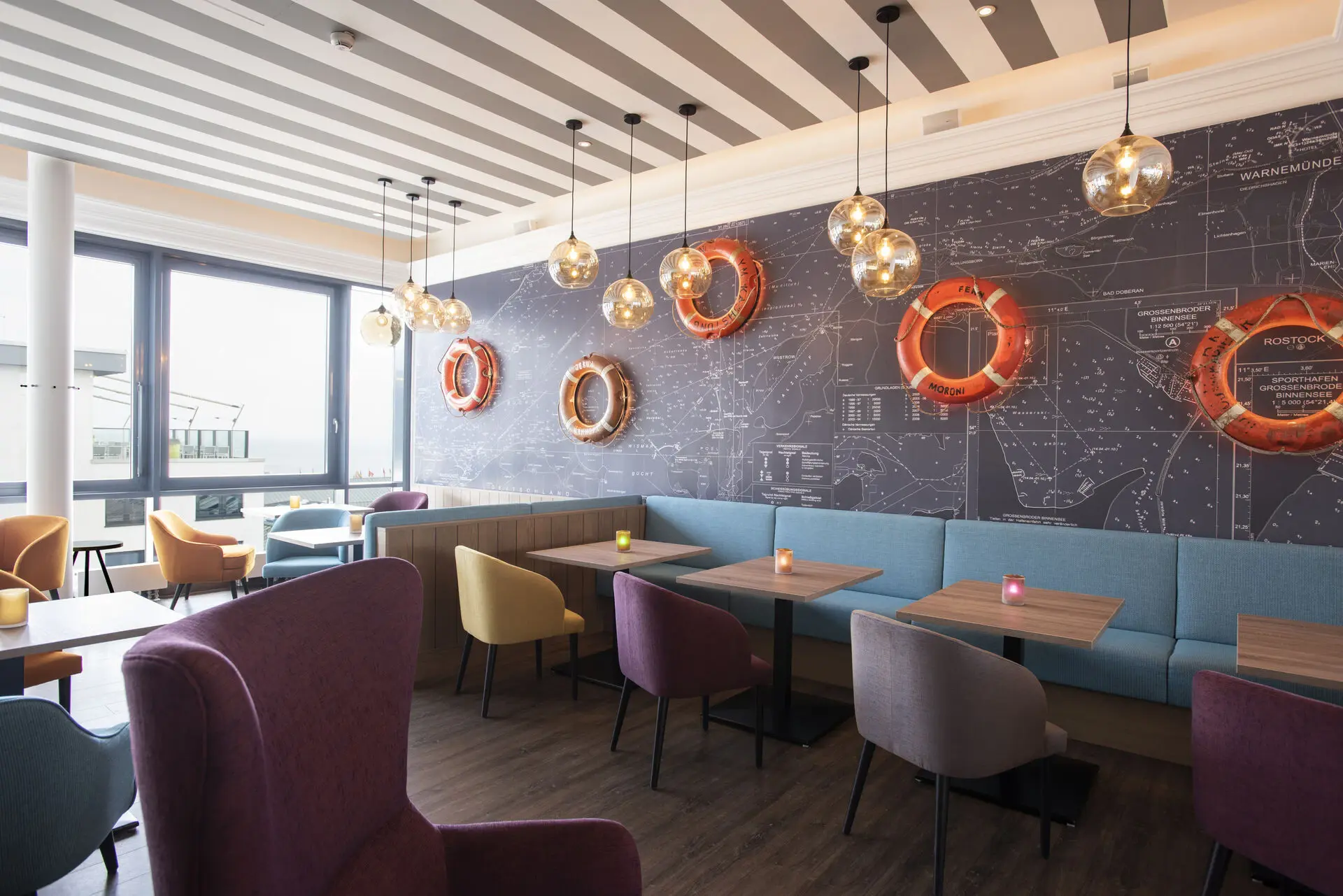 Ein Restaurantbereich mit dunklem Holzboden und Stühlen an Holztischen. An der Wand hängen orangefarbene Rettungsringe.