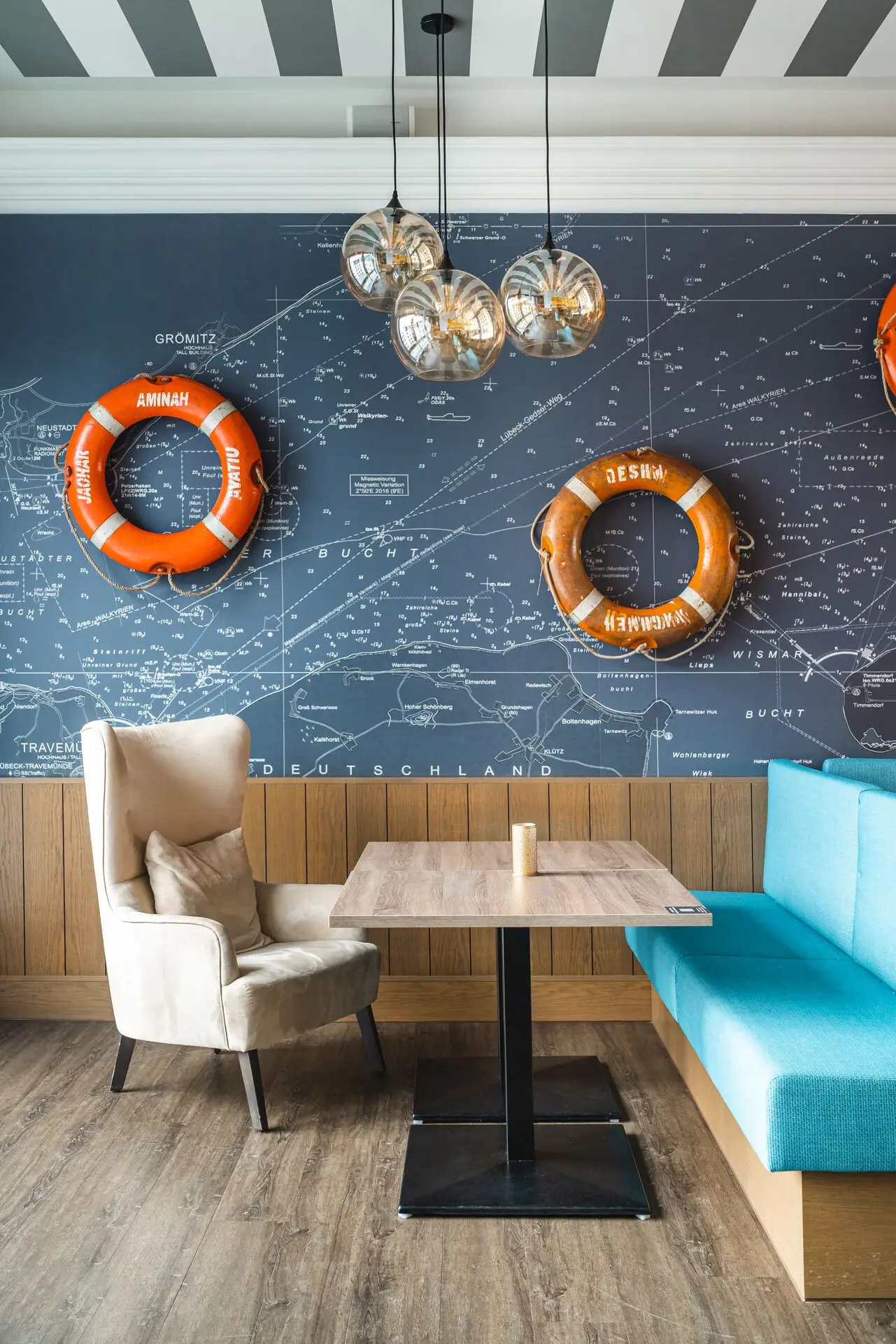 Bar im aja Grömitz Ein Tisch und Stühle neben einem blauen Sofa, mit orangefarbenen Rettungsringen an der Wand