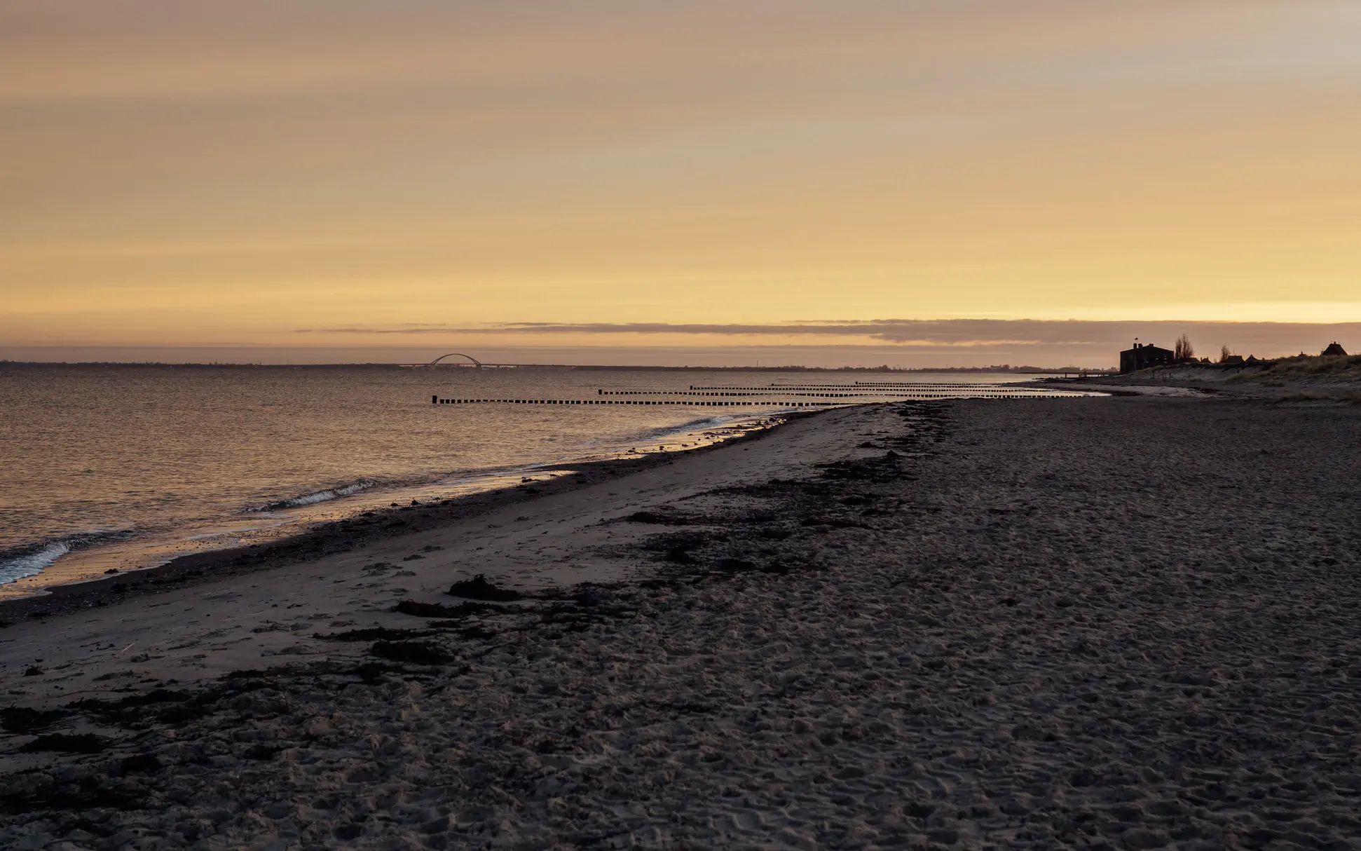 An einen ruhigen Strand schwappen leichte Wellen, während am Himmel die Sonne untergeht.