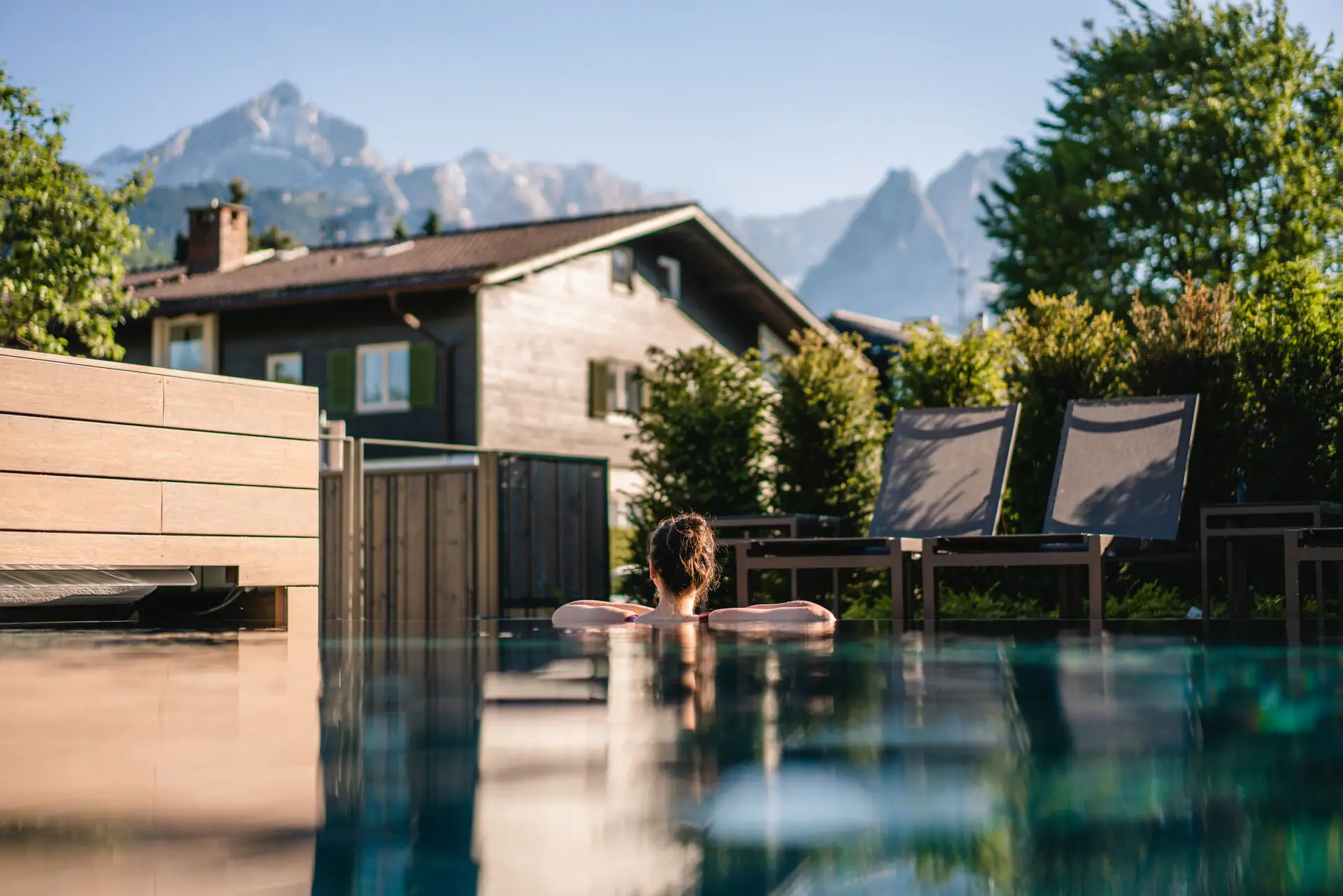 Außenpool Eine Person im Schwimmbecken mit Bäumen im Hintergrund.