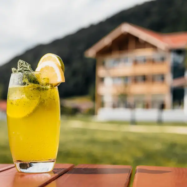 Drink im aja Ruhpolding Limonade in einem Glas und mit dem aja Ruhpolding im Hintergrund.