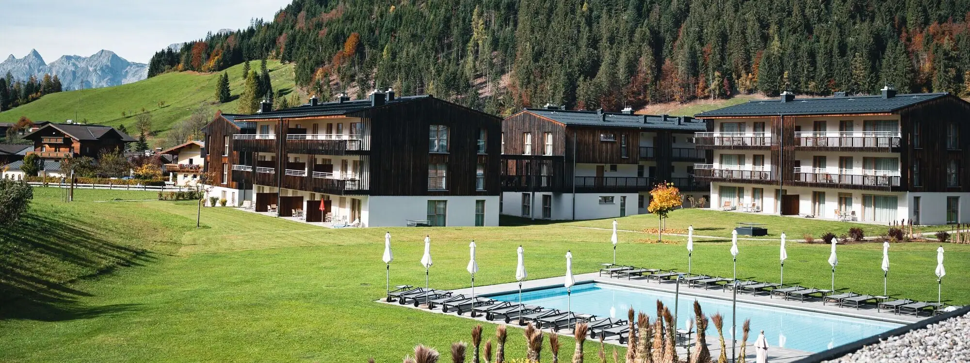 aja Ferienwohnungen Werfenweng Ein Pool vor Gebäuden mit Bäumen und einem klaren Himmel im Hintergrund.