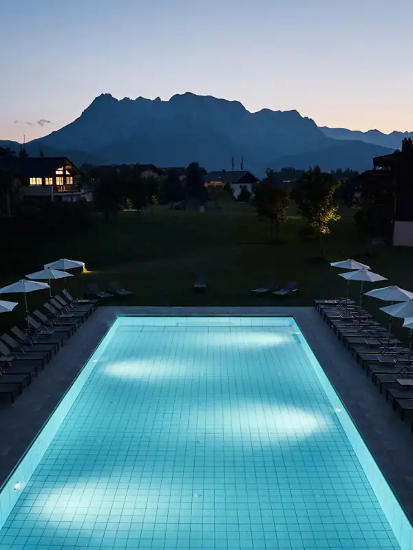 Badewelt im aja Bergresort Werfenweng Ein Pool mit Stühlen und Sonnenschirmen vor einem Haus.