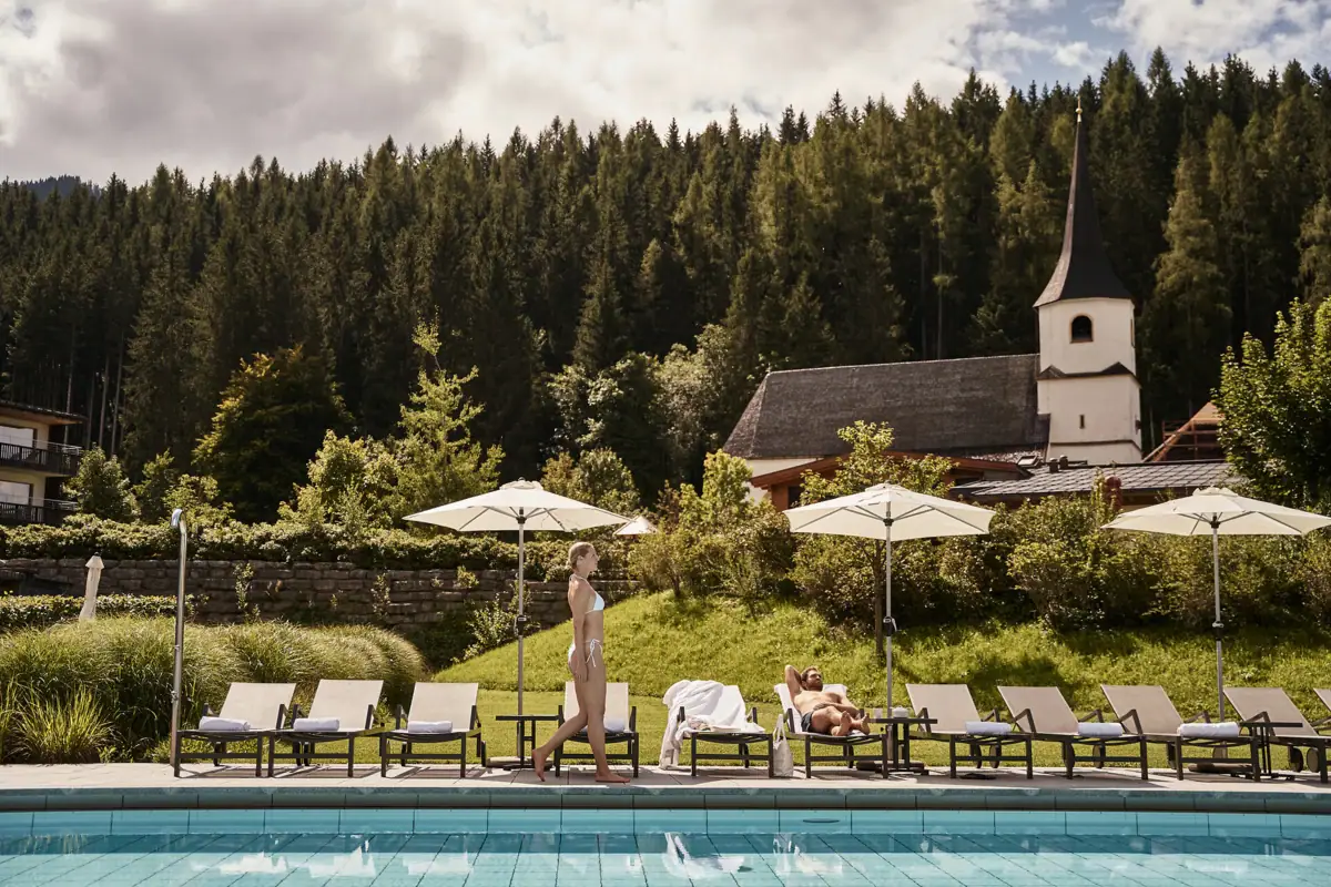 Liegen im aja Werfenweng Eine Frau geht an einem Pool entlang an dem Liegen stehen.