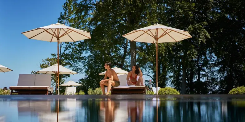 Ein Mann und eine Frau sitzen am Poolrand mit Sonnenschirmen. Ein Mann und eine Frau sitzen am Poolrand mit Sonnenschirmen.