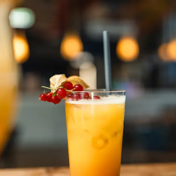 Drinks im aja Warnemünde Ein Glas mit orangenem Drink, Strohhalm und Beeren.
