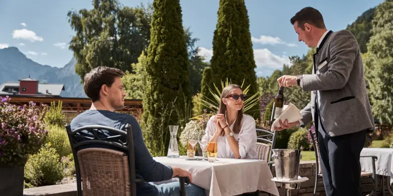 Ein Mann schenkt an einem Tisch im Freien, an dem Personen sitzen, Wein in eine Flasche. Ein Mann schenkt an einem Tisch im Freien, an dem Personen sitzen, Wein in eine Flasche.