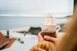 Ausblick Eine Person hält eine Tasse heiße Schokolade mit Sahne.