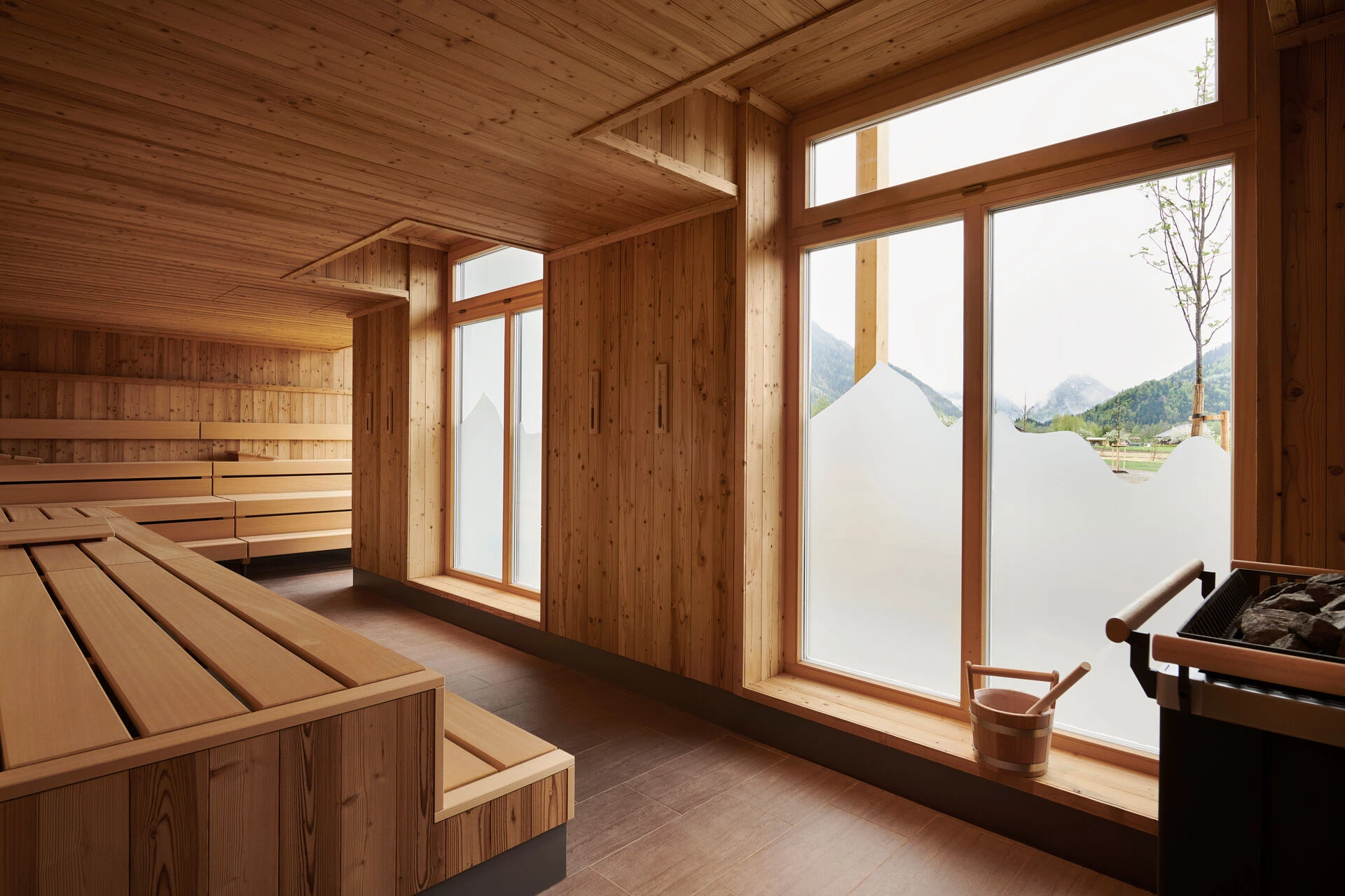 Helle Sauna mit Holzverkleidung und großzügigen Fenstern, die einen leicht getrübten Blick auf die umliegenden Berge ermöglichen.
