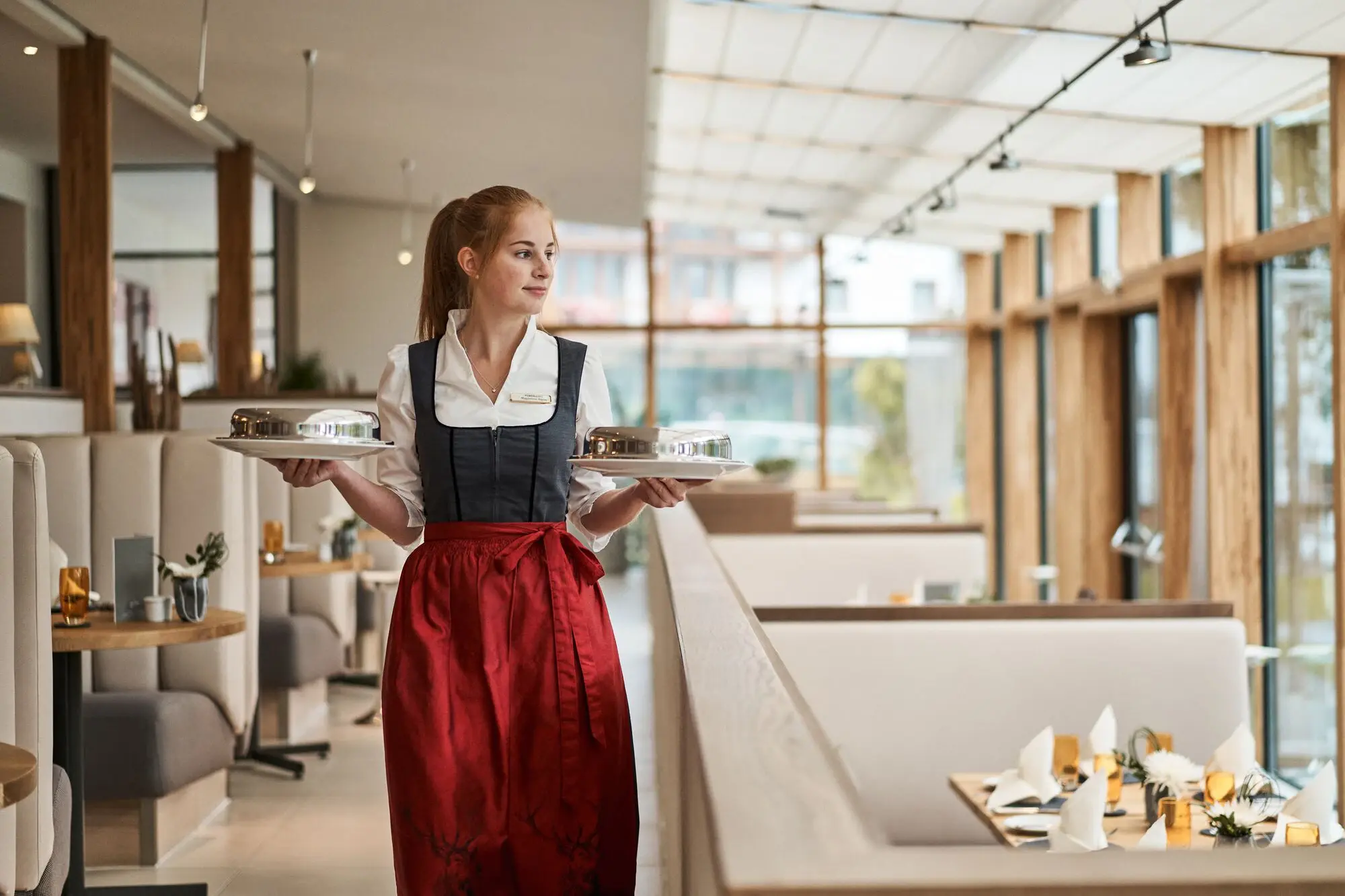 Essen im aja Fürstenhaus am Achensee Kellnerin im Dirndl hält zwei Teller während sie durch das Restaurant läuft.