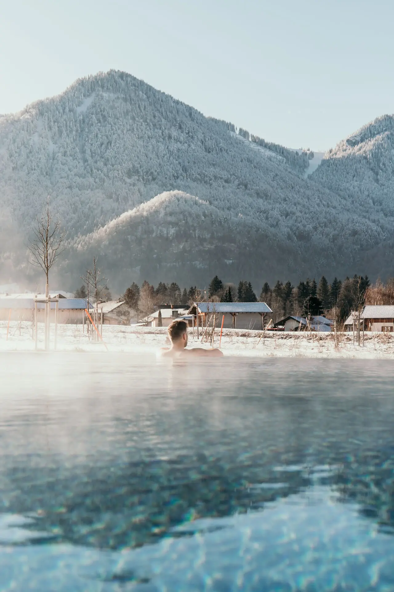 Außenpool aja Ruhpolding Ein Paar schwimmt an einem sonnigen Tag in einem Außenpool umgeben von einer Berglandschaft.