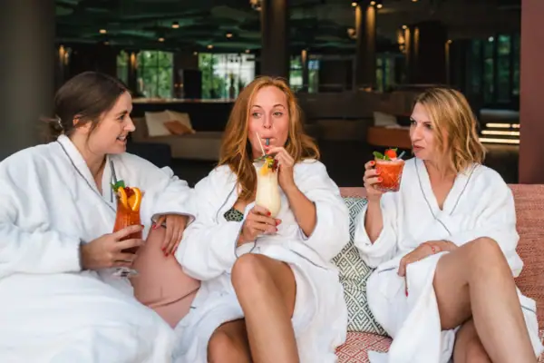 Wellnessbereich im aja Warnemünde Eine Gruppe von Frauen in weißen Bademänteln trinkt Cocktails.