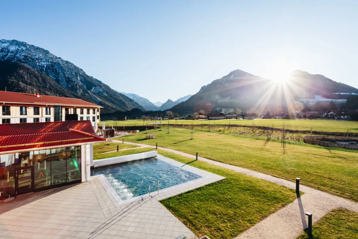 aja Ruhpolding Der Outdoor Swimmingpool vom aja Ruhpolding mit dem Golfplatz und Bergen im Hintergrund.