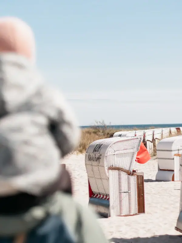 Strankörbe Eine Person mit einem Baby auf dem Rücken am Strand.
