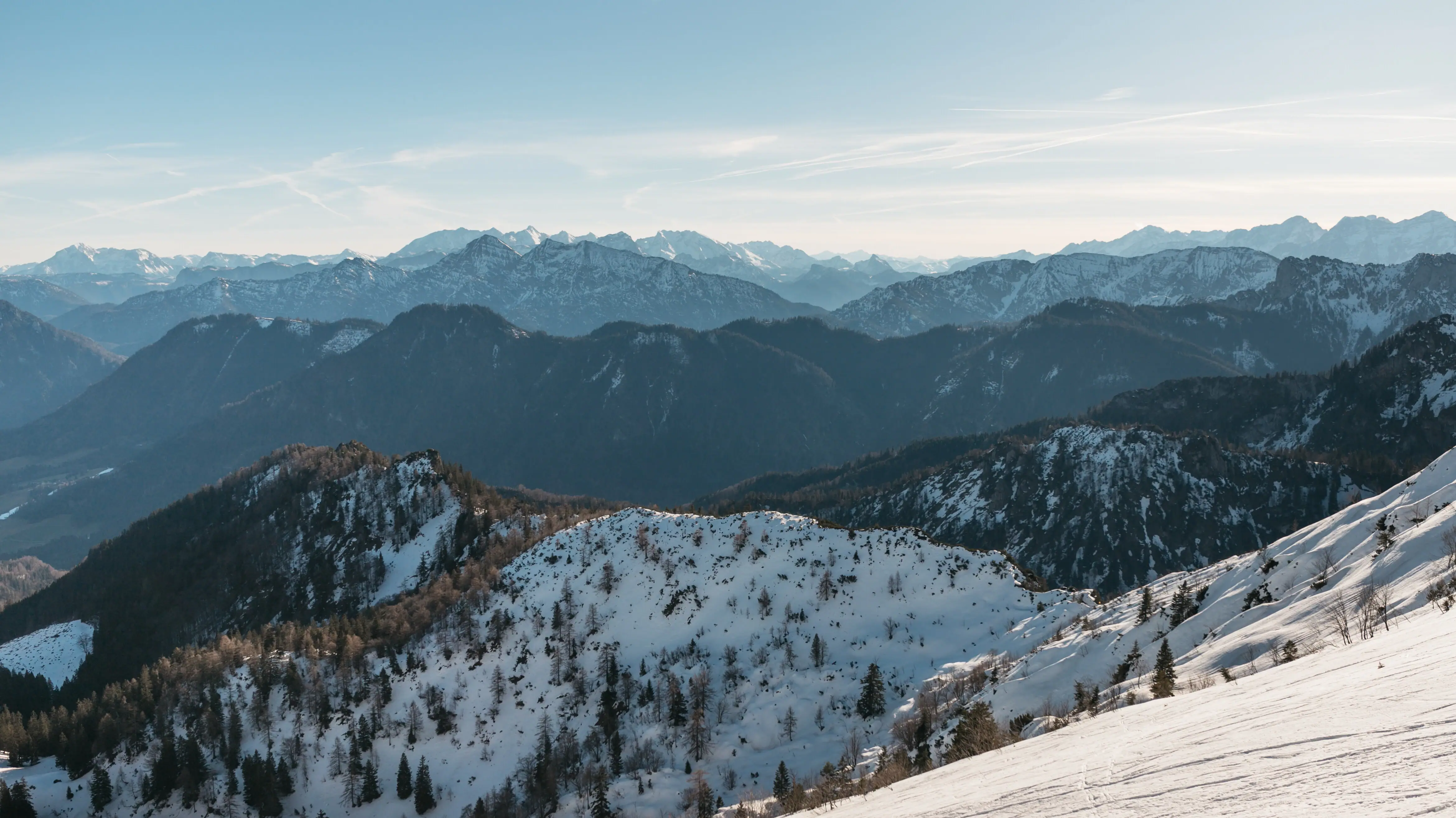 Winter in den Bergen Verschneiter Berg mit Bäumen und weiteren Bergen im Hintergrund.