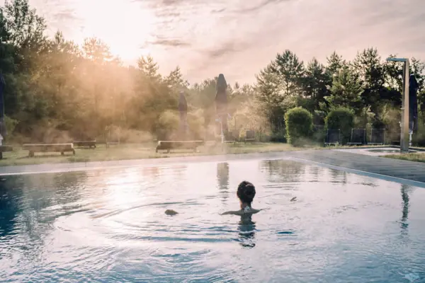 Wellness im aja Bad Saarow Eine Frau in einem Pool mit Bäumen und bewölktem Himmel.