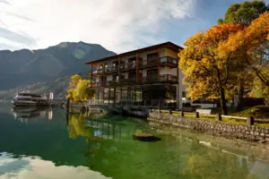 aja Fürstenhaus am Achensee Ein Gebäude neben einem Gewässer mit Bäumen und Wolken im Hintergrund.