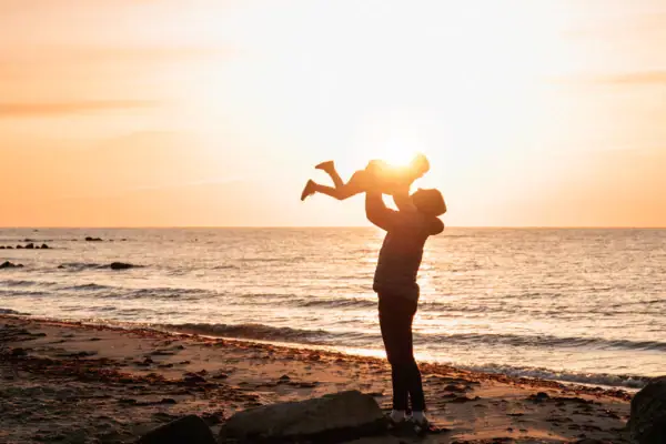 Strand bei Sonnenaufgang Eine Frau hält ein Baby am Strand.