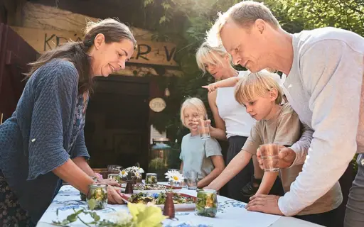 Drei Erwachsene und zwei Kinder stehen draußen um einen Tisch mit Essen herum und lächeln. Drei Erwachsene und zwei Kinder stehen draußen um einen Tisch mit Essen herum und lächeln.