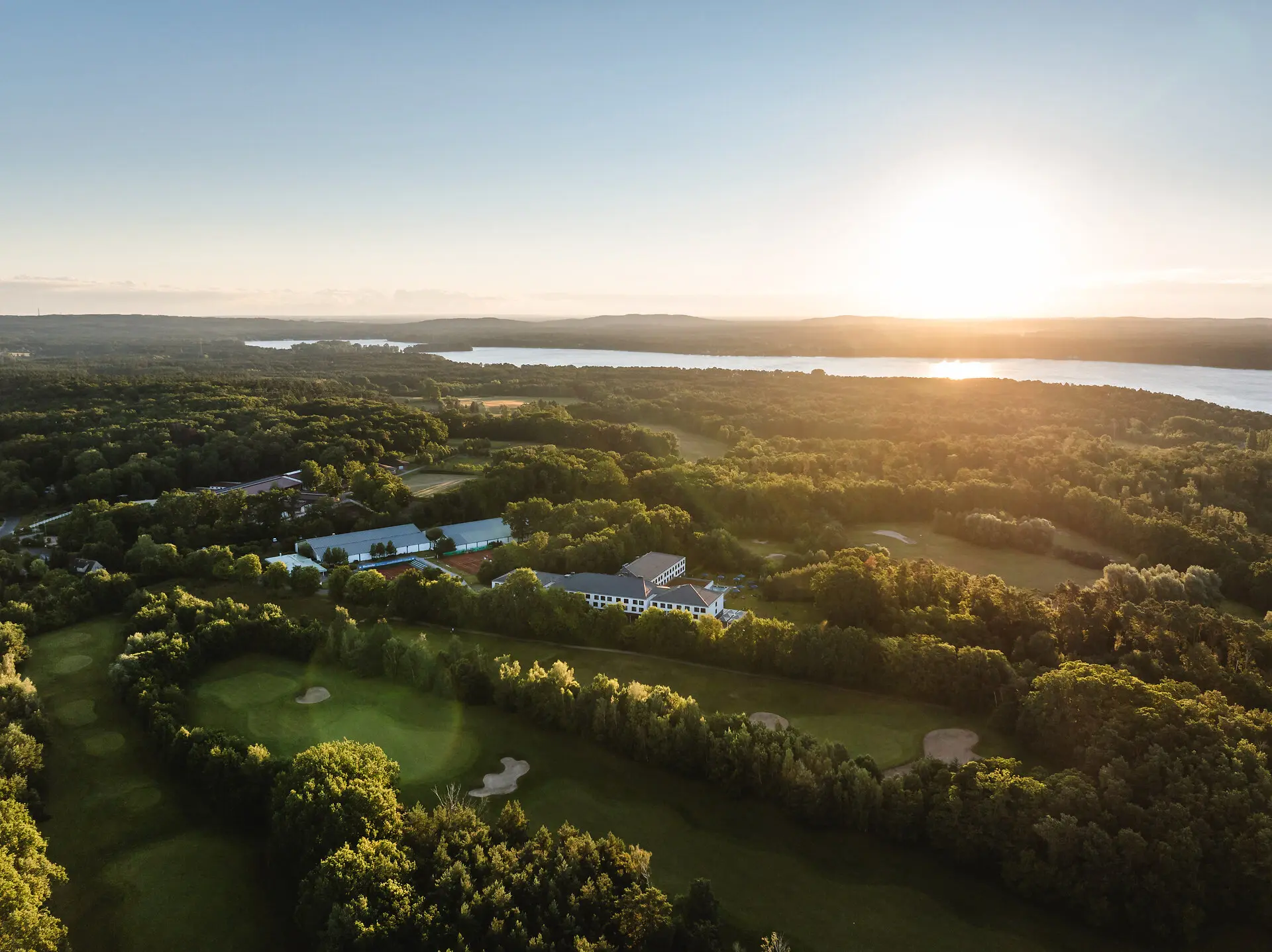 aja Bad Saarow Luftaufnahme eines Golfplatzes neben einem Gewässer bei Sonnenaufgang.