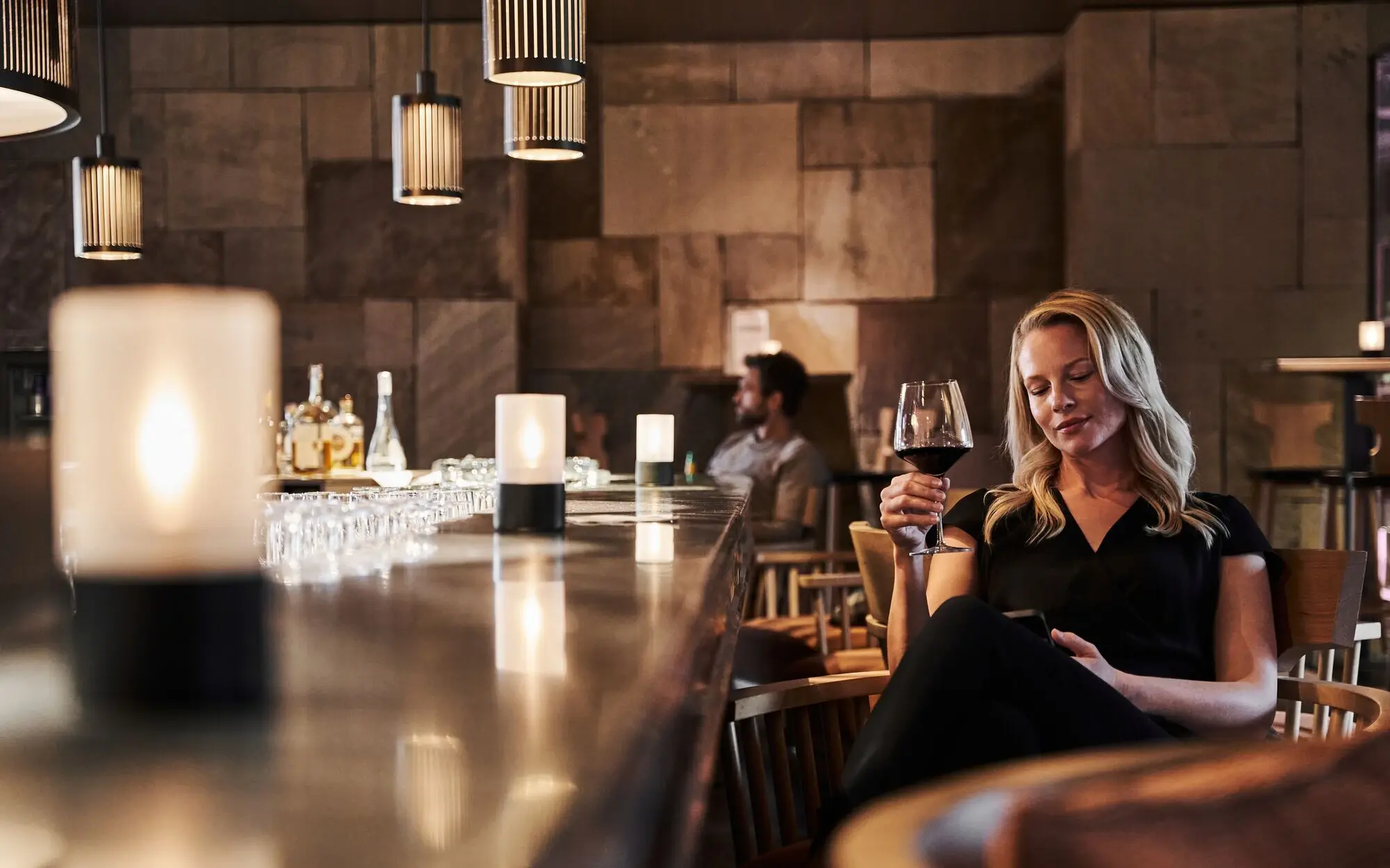 Frau sitzt an einer Bar und hält ein Glas Wein.