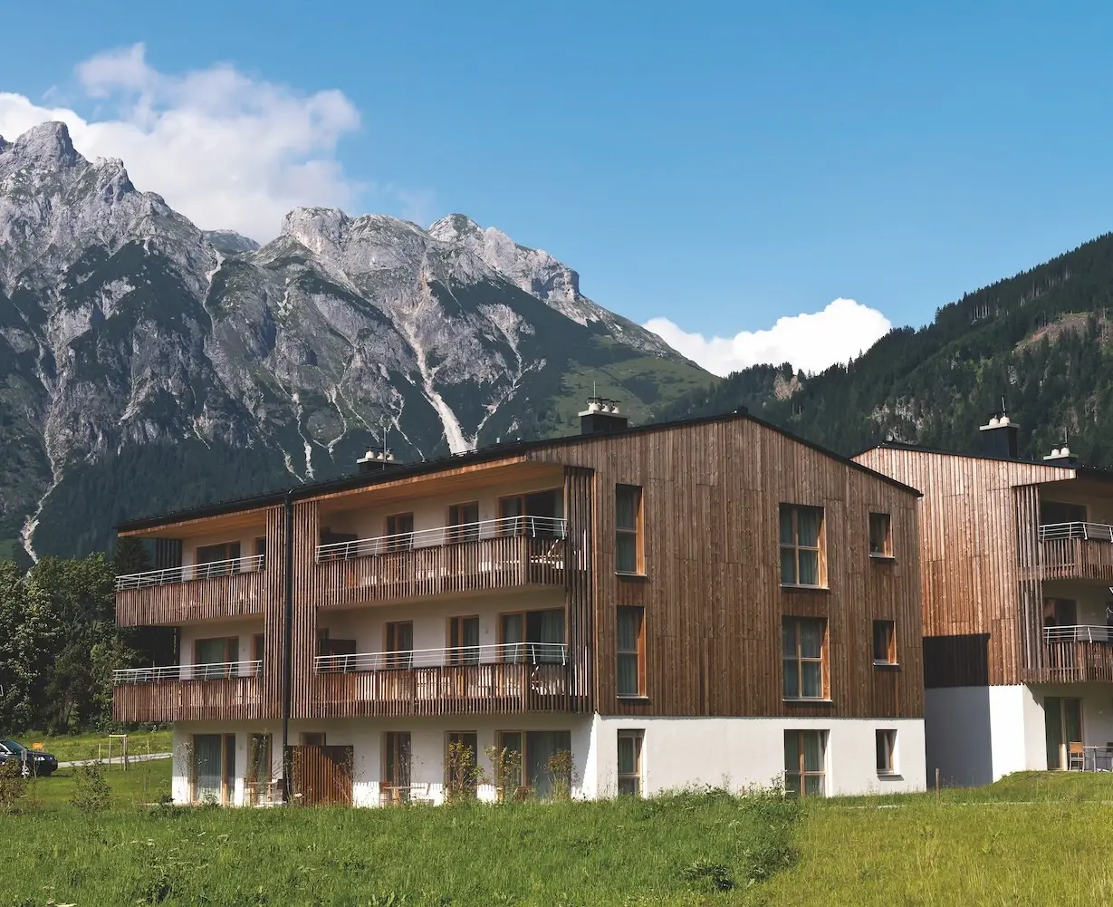Ferienwohnungen Werfenweng Gebäude mit Berg im Hintergrund und umgeben von Bäumen und Gras.