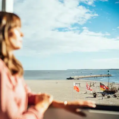 Aussicht aja Travemünde Eine Frau blickt aus einem Fenster auf einen Strand.
