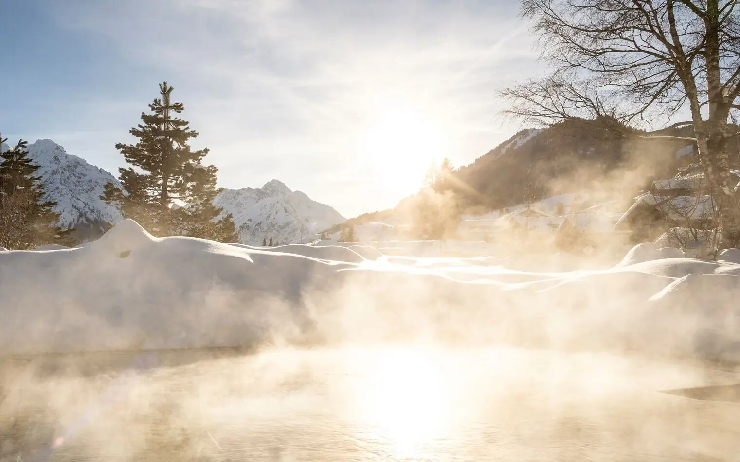 Außen Whirlpool im aja Fürstenhaus am Achensee Ein dampfender Außenpool inmitten einer verschneiten Landschaft, umgeben von schneebedeckten Bergen und Bäumen. Die Sonne strahlt hell am klaren Himmel.
