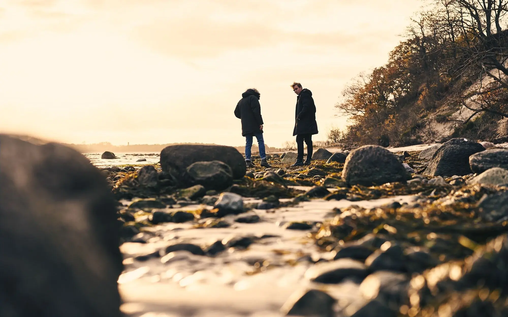 Zwei Personen stehen auf einem felsigen Strand.