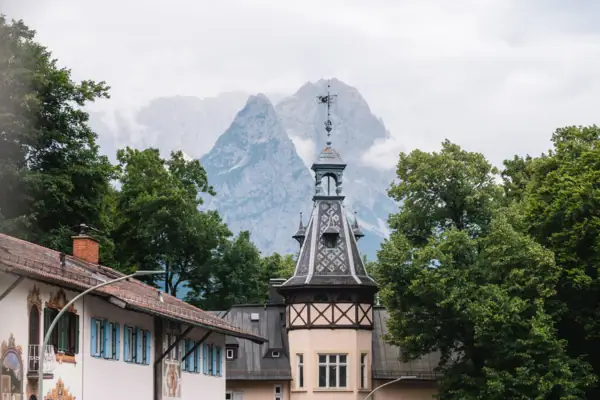 Garmisch-Partenkirchen Ein Gebäude mit einem Turm und Bäumen vor Bergen.