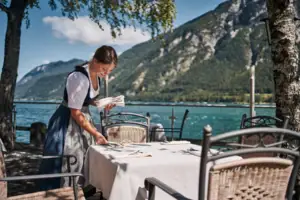 Eine Frau in einem Kleid sitzt an einem Tisch mit einem See im Hintergrund.