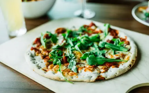 Auf einem Holzbrett wird eine Pizza mit Rucola serviert. Auf einem Holzbrett wird eine Pizza mit Rucola serviert.