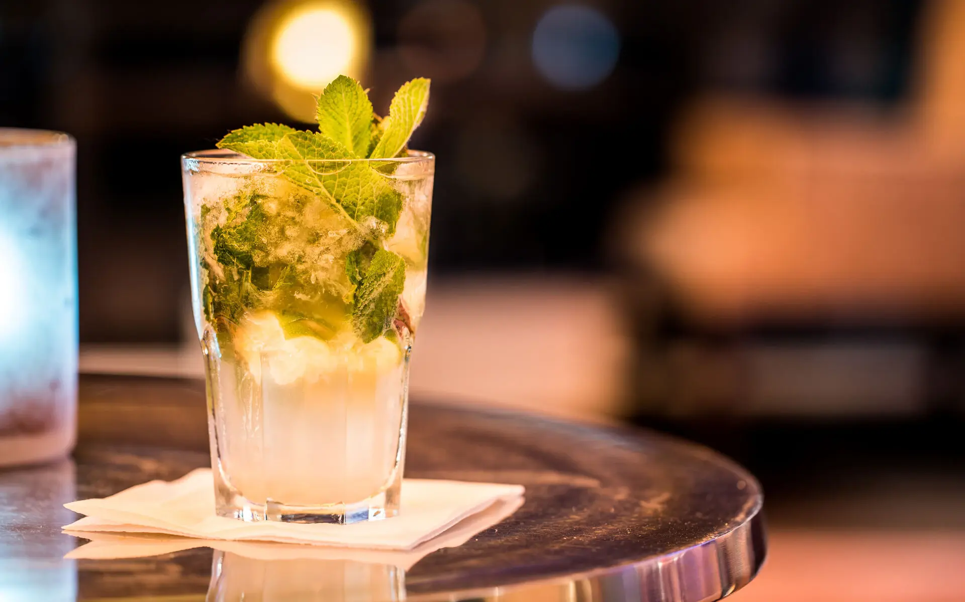 Cocktail Ein Mojito steht auf einer Servierte auf einem silbernen Tisch in einem Raum mit gedämpftem Licht.