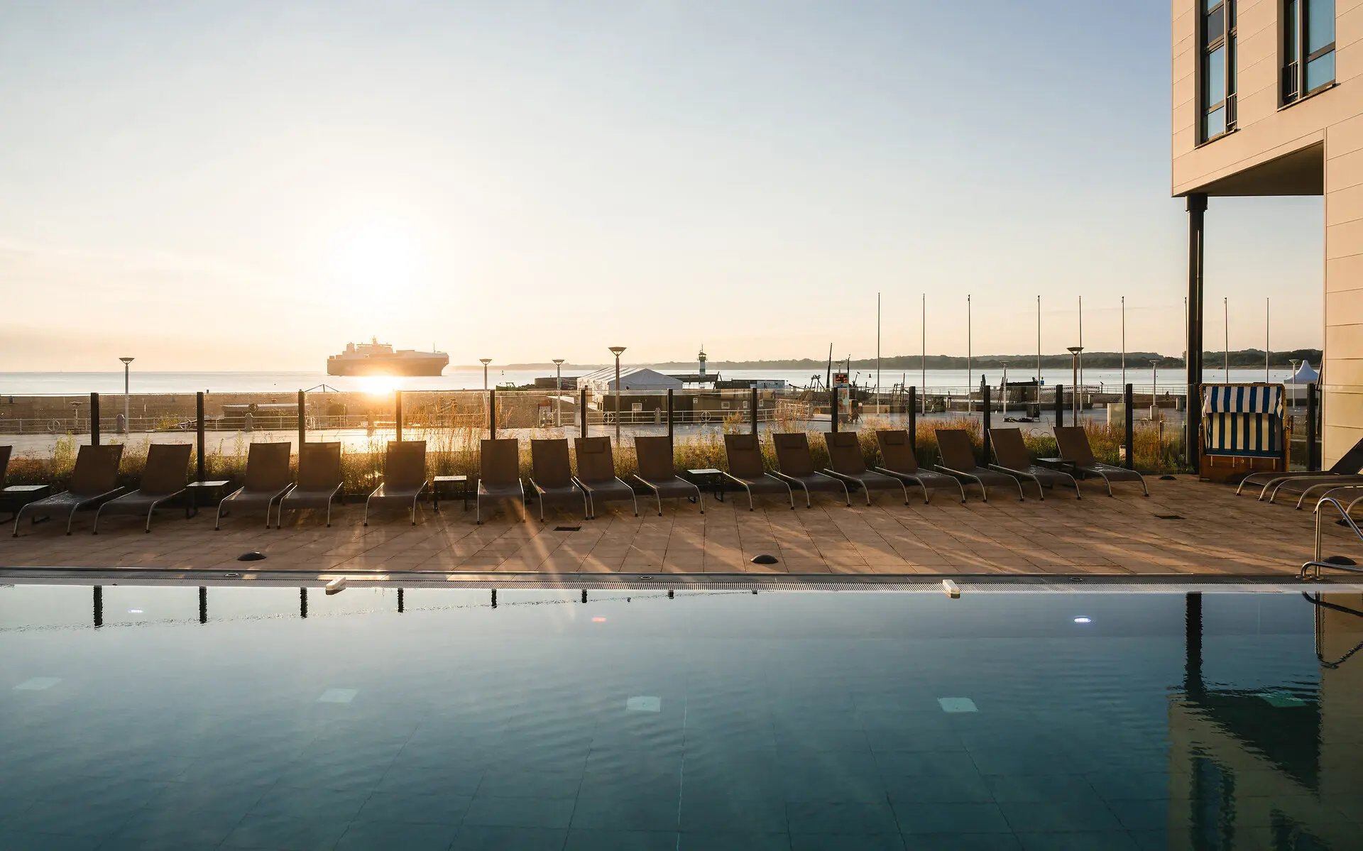 Außenpool aja Travemünde Ein Pool mit Stühlen und einem Boot im Hintergrund.