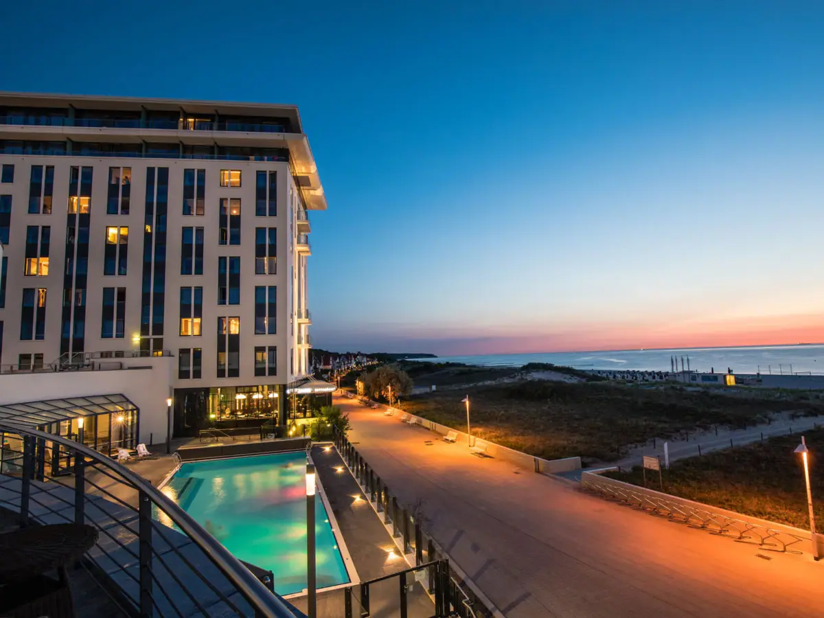 Silvester im aja Warnemünde Das Hotelgebäude mit einem Pool und einem Gehweg am Meer.
