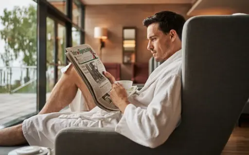Mann im Bademantel liest Zeitung auf einem Sofa. Mann im Bademantel liest Zeitung auf einem Sofa.