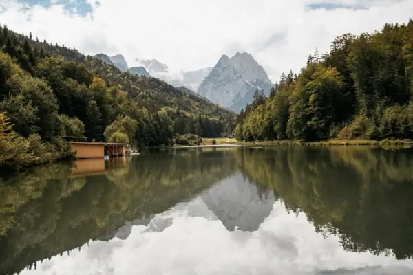 Riessersee Ein See mit einer Hütte und Bergen im Hintergrund.