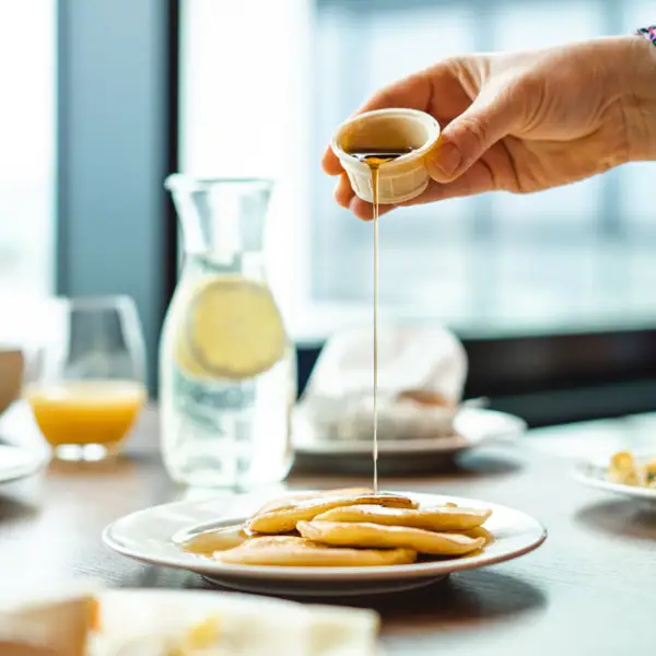 Eine Person gießt Sirup auf einen Teller mit Pfannkuchen.