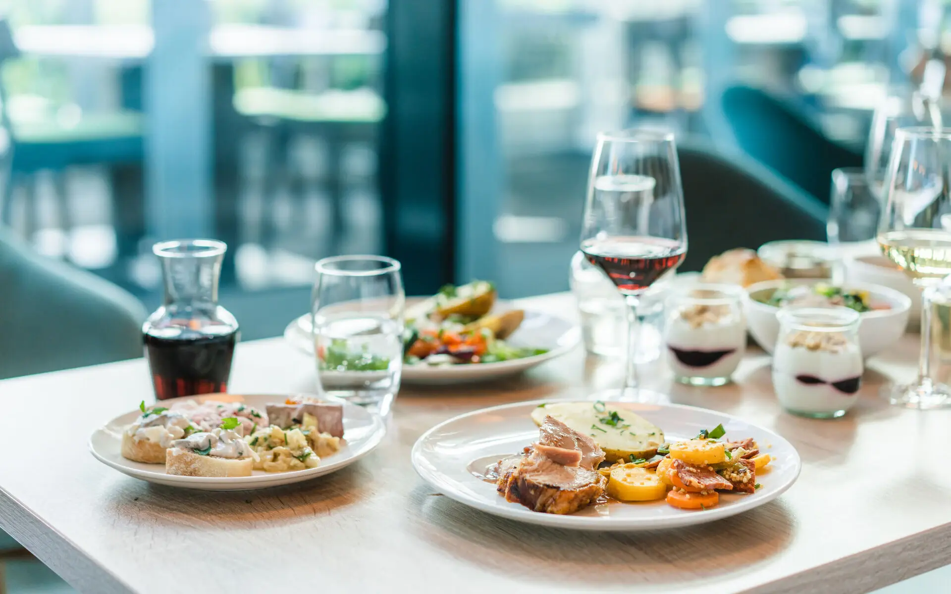 Buffetstation aja Travemünde Ein appetitlich gedeckter Tisch mit warmen Speisen von einem Buffet sowie Rotwein und kleinen Nachtischgläsern mit Quark und roter Sauce.