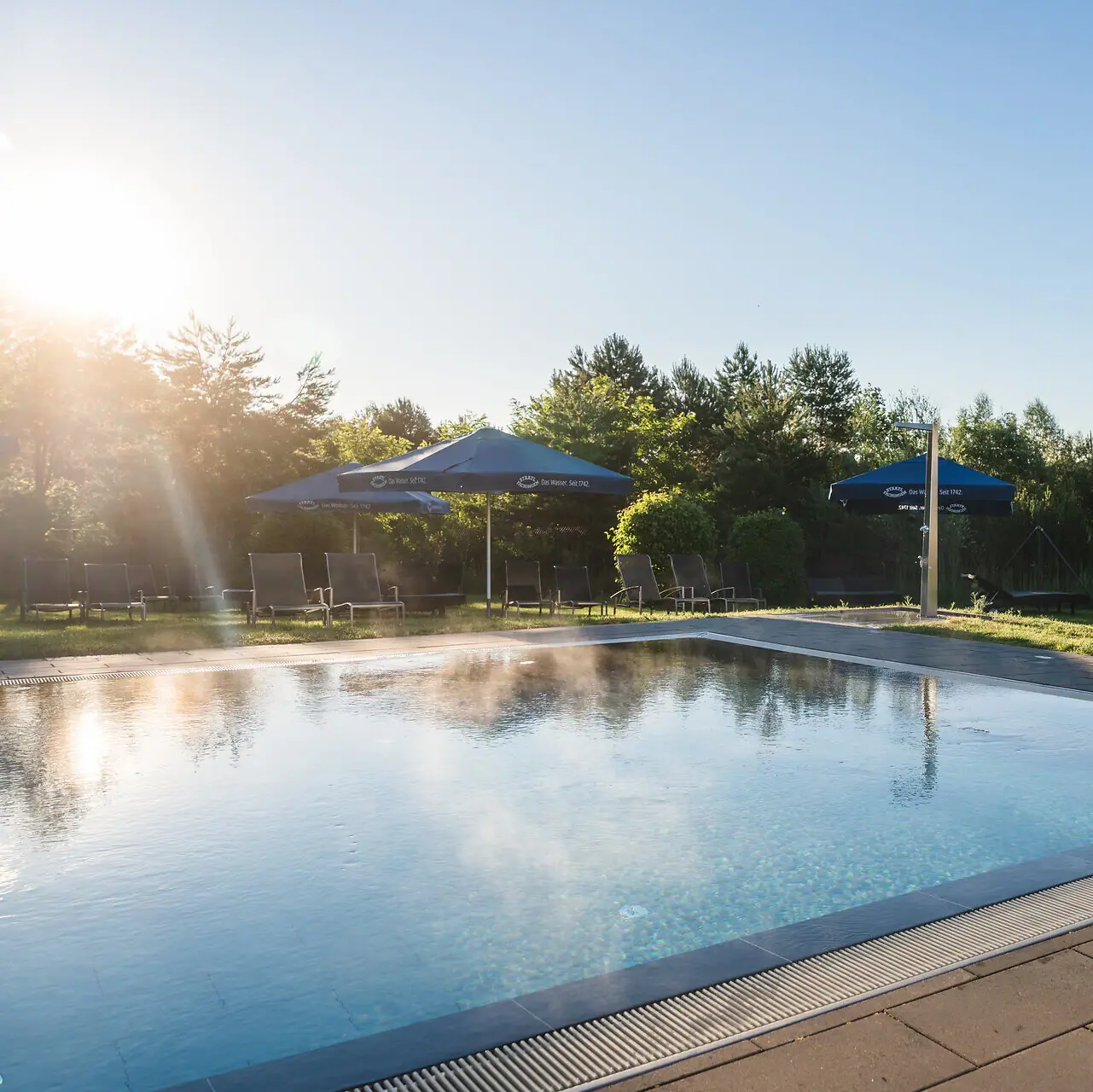Pool im aja Bad Saarow Ein Pool mit Sonnenschirmen und Gras.