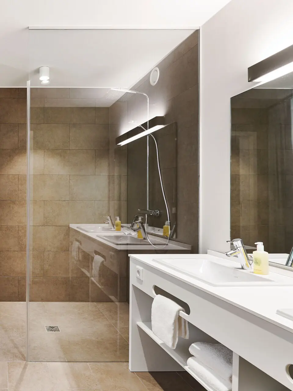 Ein modernes Badezimmer mit einem weißen Doppelwaschbecken und einer dunkel gefliesten ebenerdigen Dusche mit Glaswand.