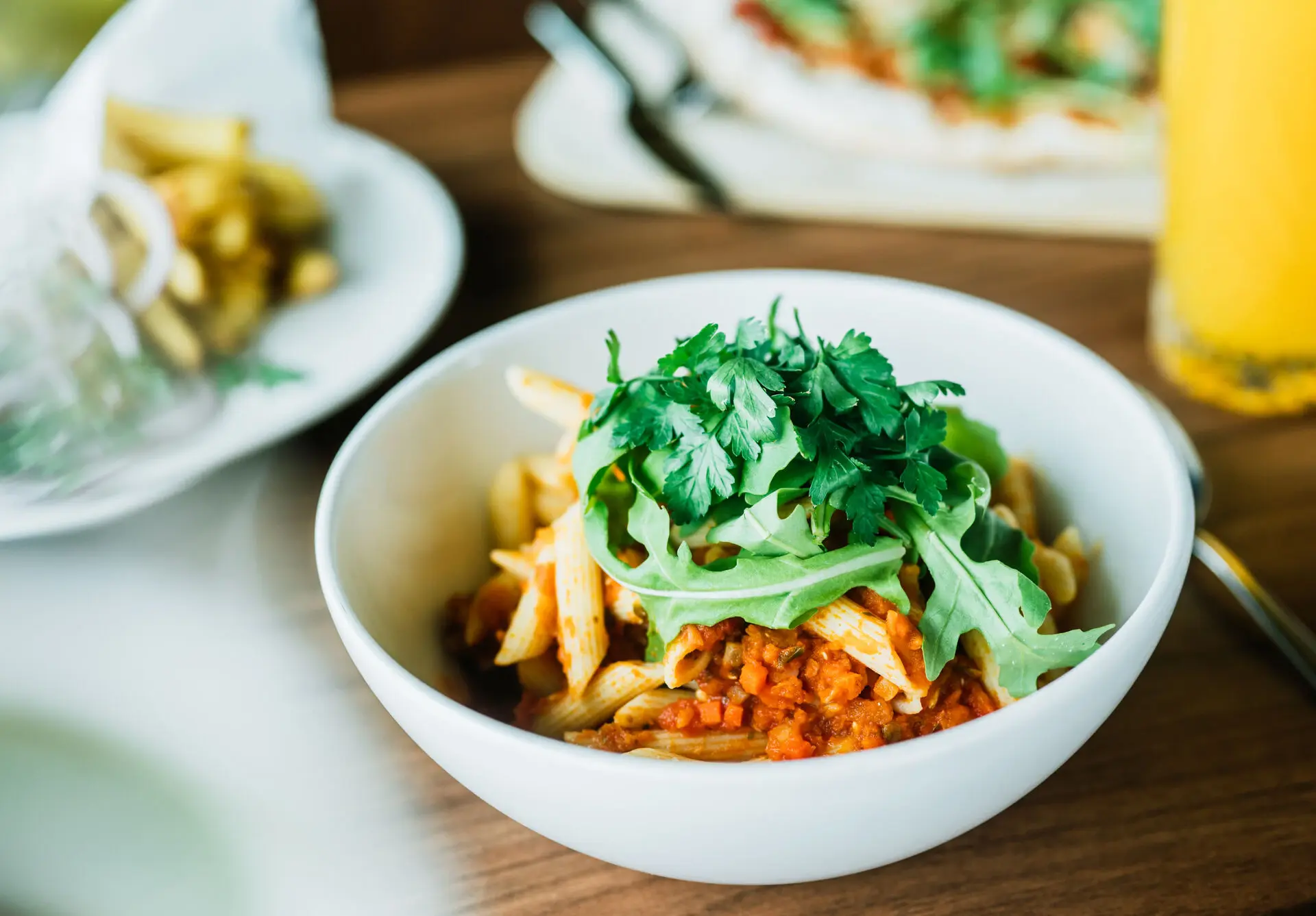 Eine Schüssel Penne mit einer würzigen Tomatensauce, garniert mit frischem Rucola und Petersilie, serviert auf einem Holztisch.
