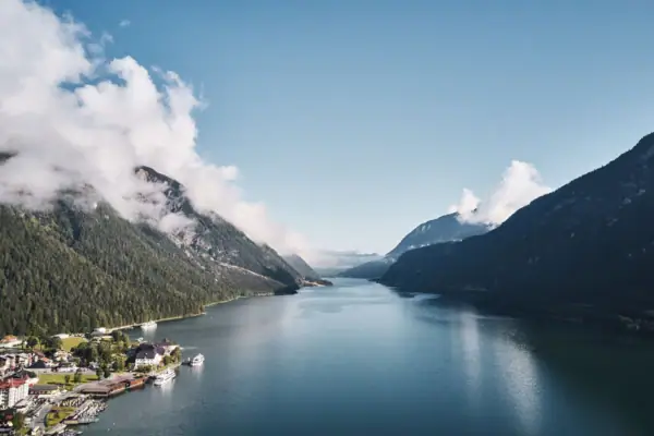 Achensee Ein Gewässer mit einem Haus und Bergen im Hintergrund.