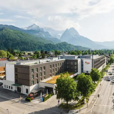 aja Garmisch Ein Gebäude mit Bäumen und Bergen im Hintergrund.