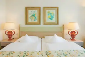 Juniorsuite seeseitig mit Balkon Ein Bett mit zwei Lampen und zwei Bildern an der Wand.