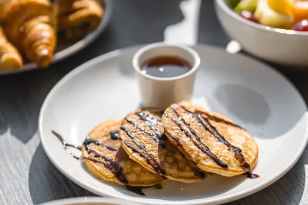 Eierspeisen Ein Teller mit Pfannkuchen und Sirup sowie eine Tasse mit Sirup.