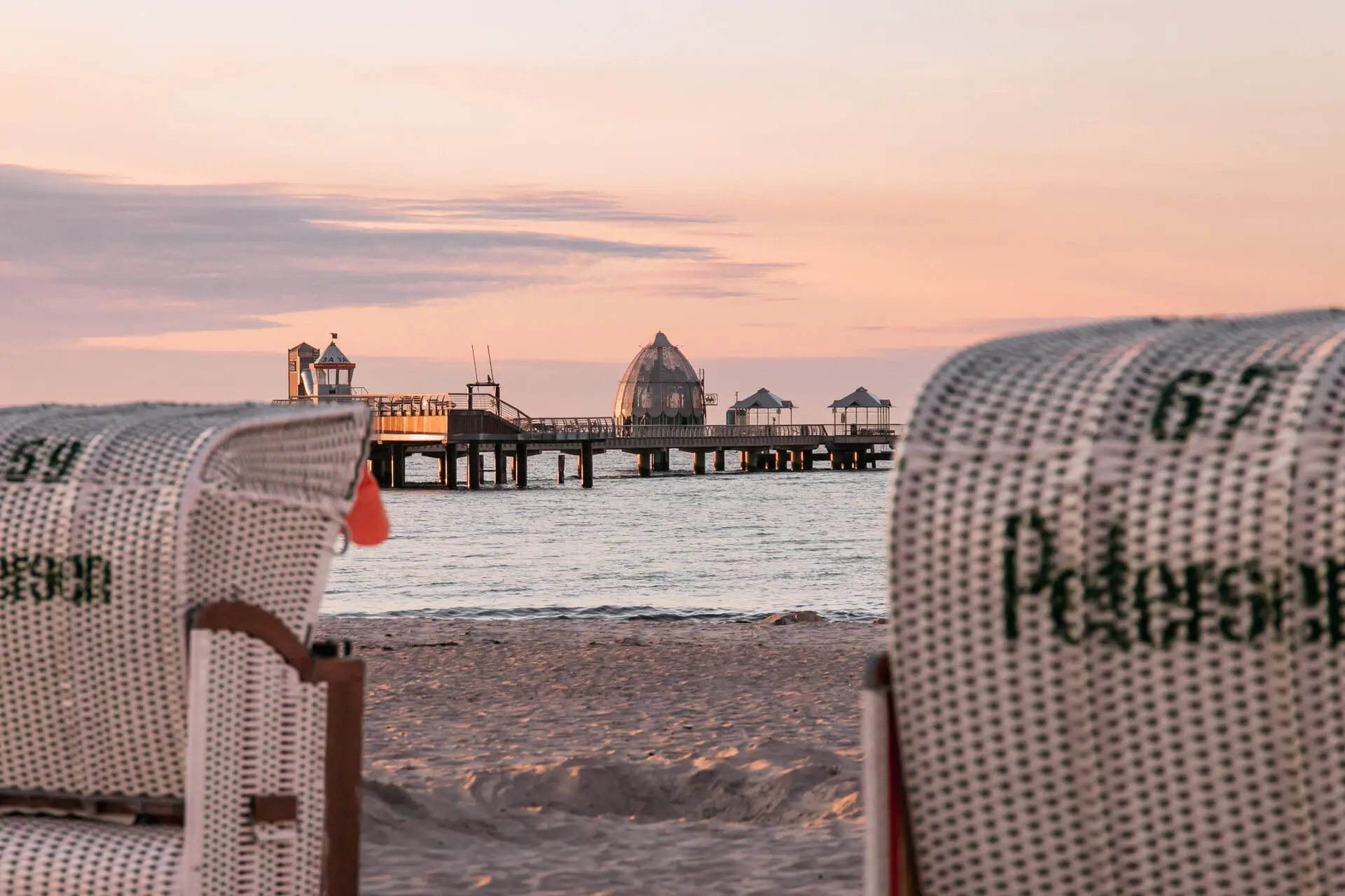 Ein Strandkorb am Strand mit einem Pier im Hintergrund.