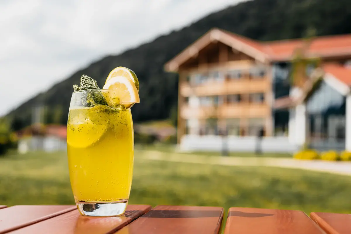 Ein Glas mit gelber Flüssigkeit, garniert mit einer Zitronenscheibe und Minze, auf einem Tisch.